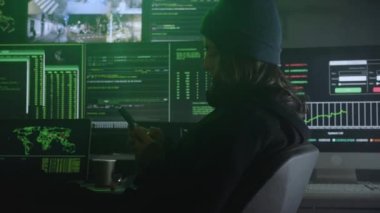 Bilgisayarlar finans sektörü ve bankacılık sektöründeki büyük şirketlerin sunucularına büyük çaplı veri hırsızlığı yaparken cep telefonu kullanan kadın hacker. Karanlık odadaki kadın. Gizli suçlular..