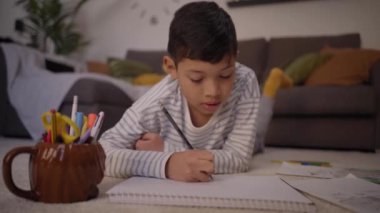 Küçük Latin çocuk evdeki oturma odasında sessizce resim çiziyor. Konsantre çocuk hafta sonu okul ödevi yapıyor. Tatillerde çocuk aktiviteleri ve çocuklukta aile boş zamanı kavramı. 