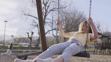 Mutlu küçük sarışın kız, güneşli bir sonbahar gününde parktaki salıncakta sallanırken gülümseyen kameraya bakar. Sevimli küçük aşk kızı parkta ailesiyle dışarıda eğleniyor..
