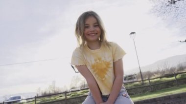 Gülümseyen küçük beyaz kız güneşli bir günde açık havada kamera aşk ifadesine bakıyor. Şirin kıkırdayan sarışın çocuk parkta video izlemek için yaramaz poz veriyor. Aile ve boş zamanlardaki çocukluk kavramı.