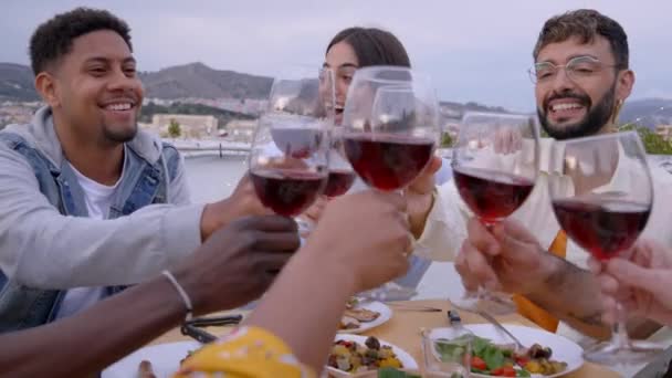 夜にはテラス席でワインを飲みながら多彩な陽気な人々が乾杯 夏には屋上で幸せなディナーをお祝いする若い友達が集まります 社会化と地中海料理 — ストック動画