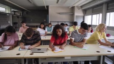 Sınıfta oturmuş notlar alan konsantre bir grup üniversite öğrencisi. Lise öğrencileri başlarını kaldırıp kameraya bakıyorlar. Eğitim toplumu insanları ve Z nesli. 