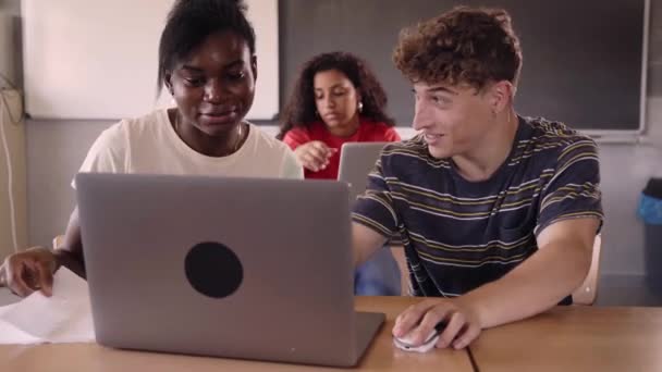 2人の若い多人種の学生は 大学の教室でラップトップを使用して科目を勉強します 机に座っている同級生のペアとセミナーについて一緒にチャット Z世代だ 男の子と女の子 — ストック動画
