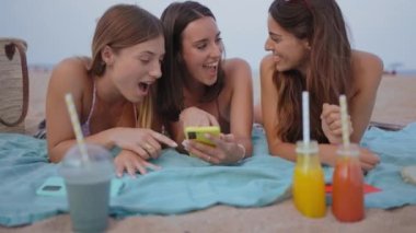 Sahilde cep telefonu uygulaması kullanan gülümseyen üç genç kadından oluşan bir grup. Neşeli kızlar hafta sonunun keyfini çıkarıyorlar. Z kuşağındaki yaz tatili, arkadaşlık ve sosyal ağ kavramı.