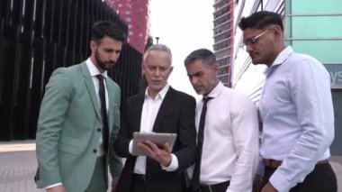 Çeşitli erkek profesyonellerden oluşan ekip, takım lideri tabletine yoğunlaştı. İş arkadaşlarının ciddi ifadeleri dijital ekran kullanılarak iş binasının dışında toplandı. Dışarıdaki kendine güvenen ofis çalışanları..