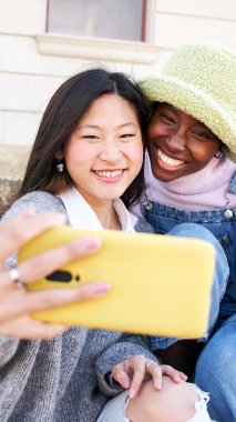 İki neşeli bayan arkadaşın dikey gülümseyen selfie 'si eğleniyor. Akıllı cep telefonuyla fotoğraf çeken ırklar arası bir çift. Mutlu insanlar sadece kızlar için tatillerden zevk alır. Yüksek kalite fotoğraf