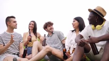 Yaz kıyafetleri içinde bir grup neşeli arkadaş sahilde bira şişeleriyle kadeh kaldırıyorlar. Arkadaşlık ve toplum konsepti. Yüksek kalite 4k görüntü
