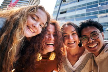 Fotoğraf çeken bir grup arkadaş kameraya bakıp gülümsüyor. Dışarıda durup eğlenen genç insanlara gülüp eğlenmek. Şehirde eğlenen dört genç kızın portresi.