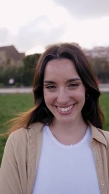 Kameraya bakıp gülümseyen bir kadının dikey portresi. Güzel kız mutlu ve sevimli ve pozitif bir ifadeyle poz veriyor. Çekici ve kendine güvenen beyaz kadın dışarıda eğleniyor.