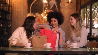 Üç tane gülümseyen çok ırklı arkadaş bir kafede yıldönümü hediyesi veriyorlar. Kadınlar arkadaşlarına kahve içerken hediye verirler. Mutlu ve hoşnut genç insanlar beklenmedik ve yararlı detaylar alıyorlar.