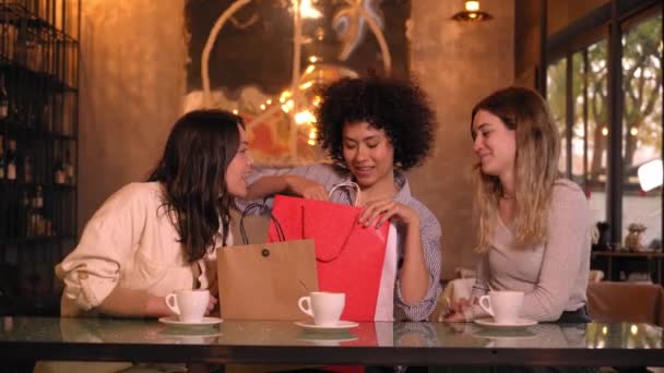 三个微笑的多种族朋友在咖啡店里送结婚周年礼物 女人在喝咖啡时送给朋友一份礼物 快乐而满足的年轻人得到了意想不到的有用细节 — 图库视频影像