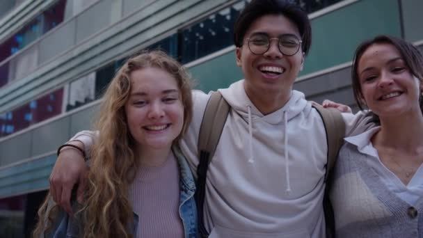 エラスムスの留学生がカメラを見て喜んで屋外で抱き合っています 写真のポーズを4人の笑顔の若い友人のグループ ヨーロッパを旅する陽気な人々 — ストック動画
