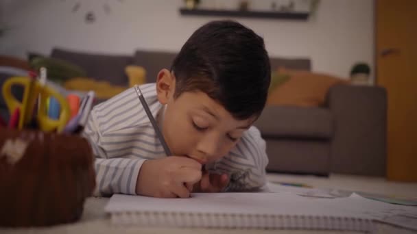 ラテン語の少年は リビングルームのノートブックの宿題絵画に焦点を当てました 自宅のカーペットの上の子供たちは自由時間に絵を描いています エンターテイメントとキッズ開発のコンセプト — ストック動画