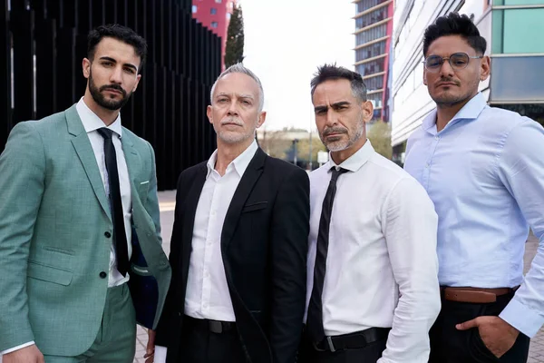 Team portrait of diverse male professionals confident posing outside business center. Group of serious middle aged formal working men looking at camera outdoor office. Photo of elegant co-workers.