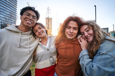 Açık havada eğlenen dört öğrencinin portresi. Sarılıyorlar. Fotoğraf üniversitenin kampüsünün dışında çekildi. Çok mutlu görünüyorlar ve kameraya bakıyorlar..