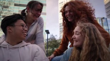 Çoklu etnik gruptan genç arkadaşlar dışarıda sohbet edip gülüyorlar. Zincirlenmiş öğrenciler birbirlerine sarılıp heyecanlı konuşuyorlar. Z neslinin neşeli insanları bir araya gelip topluluk içinde eğleniyorlar..