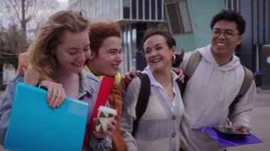 Şehir caddesinde mutlu mesut yürüyen dört genç arkadaşın fotoğrafı. Güneşli bir günde gülümseyen ve eğlenen öğrenciler. Erasmus neşeli sınıf arkadaşı üniversiteliler kucaklaşıyorlar..