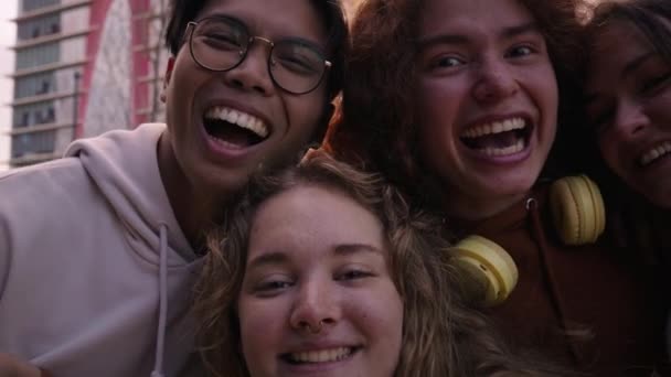 カメラを見て笑顔の写真を撮る友人のグループ 外に立って楽しんでいる若者を笑う 市内で楽しんでいる4人の十代の男女の肖像画 — ストック動画