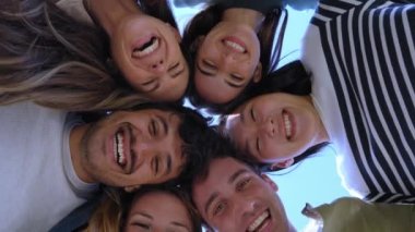 Çemberde bekleyen ve kameraya heyecanla gülümseyen çok ırklı genç insanlardan oluşan bir grup. Mutlu nesiller z arkadaşları kucaklaşırken eğleniyor. Düşük açılı, güneşli, açık hava portresi.