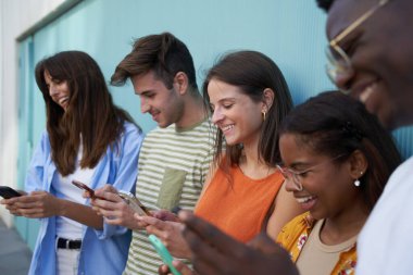 Bu teknolojiye bağımlı gülümseyen bir grup genç insan cep telefonu kullanıyor. Dışarıda durup cep telefonlarına bakıyorlar. Sosyal medyada sohbet ediyorlar..