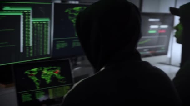 ラップトップを使ってサイバー攻撃を組織し 大企業から機密情報を盗み 身代金を要求する2人の犯罪ハッカーのチーム コンピュータに囲まれた暗い部屋で働く人々 — ストック動画