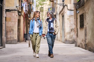 Mutlu yetişkin Kafkasyalı çift, şehirdeki güzel turist caddesinde el ele dolaşıyorlar. Olgun insanlar romantik bir tatil yürüyüşünün tadını çıkarıyorlar. Pozitif ilişkiler ve hafta sonu kaçamakları ilkbaharı.