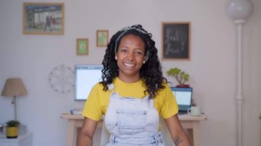 Ofiste oturan neşeli siyahi serbest meslek sahibi kadın portresi. Güzel, gülümseyen, kollarını kavuşturarak kameraya bakan Afro-Amerikan bir kız. Çevrimiçi işi olan girişimciler.
