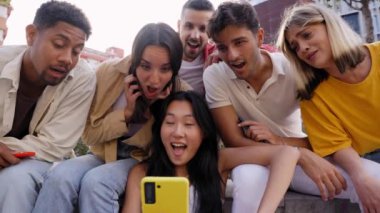 Grup gençleri telefonda bir şey izlerken şaşırdılar. Dışarıda oturan çok ırklı arkadaşlar birlikte cep telefonu kullanıyorlar. Yeni nesiller için arkadaşlık sosyal ağları ve teknoloji bağımlılığı kavramı.