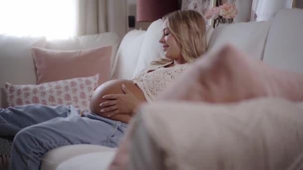 Relaxed Pregnant Blonde Woman Gently Strokes Belly Sitting Sofa Home — Stock Video