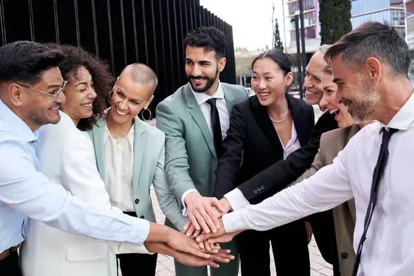 Multicultural happy business formal group team building joining hands. Smiling smart diverse professional people enjoy success outside office center. Fellowship and positive relationships at work.