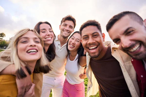 Multiracial people happy group smiling at camera for photo outdoors on sunny day. Diverse laughing young friends enjoy together hugging. Positive friendship relationships in diverse community.