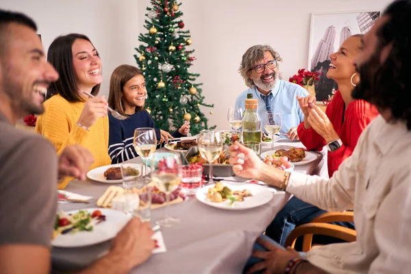 Funny family gathering celebrating Christmas vacations together at festive table. People laughing and eating together at home on Thanksgiving Day. Three Caucasian generations enjoying domestic life.