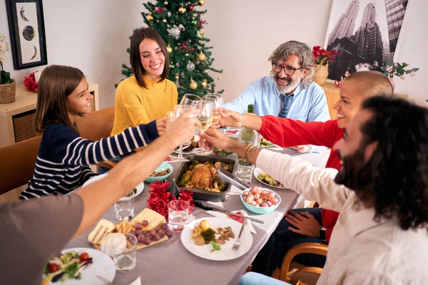 Happy Caucasian family celebrating winter vacations together drinking white wine at festive table. Joyful people toasting at Christmas gathering. Three generations enjoying domestic life smiling.