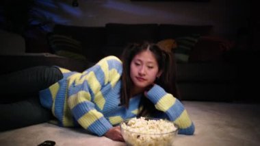 Asyalı rahat kadın oturma odasındaki halıya uzanmış, elinde patlamış mısırla ciddi bir şekilde yatıyor. Genç nesil Z dişileri televizyonu açar ve geceleri evde film veya dizi izlemekten zevk alır. İnsanlar ev yaşamında dinleniyor