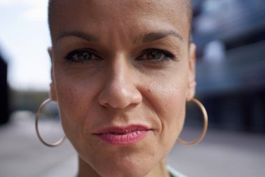 Kameraya bakan orta yaşlı beyaz kadın portresi. Ciddi bir Avrupalı kadın dış mekanda kendine güveniyor. Tıraşlı, kafası tıraşlı, beyaz, samimi bir yüz ifadesi. Kırklı yaşlardaki insanlar.. 