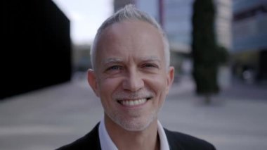 Gülümseyen olgun iş adamı ofis binasının önünde kameraya olumlu bakıyor. Yönetici CEO profesyonel yönetici kendine güveniyor. Mutlu gri saçlar resmi çalışan erkekler