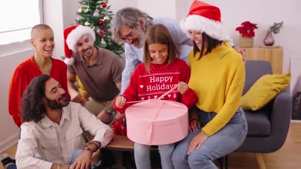 自宅でクリスマスプレゼントを開く驚いた少女 サンタクロースの帽子をかぶった幸せで興奮した家族がギフト交換のために集まった 冬季休暇中のポジティブで楽しい国内関係 — ストック動画