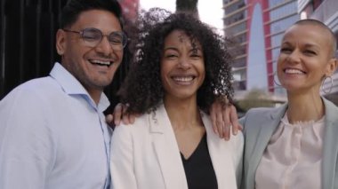 Üç iş arkadaşı dışarıda gülen kameralara bakarak poz veriyor. Ofis dışında gülümseyen çok ırklı insanlar. Resmî neşeli reklamcılar profesyoneller ve pozitif iş ilişkileri.