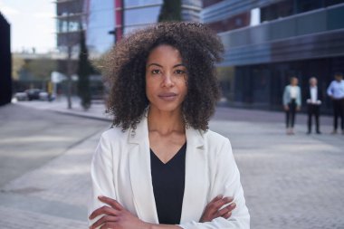 Orta yaşlı Afro-Amerikan iş kadınının kamera kolları çaprazlanmış bir portresi. Kendine güvenen bir kadın resmi olarak ofis dışında afro saç pozu verir. Uzay personelini ciddi kişiler olarak kopyala.