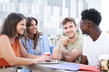Üniversitenin barında sohbet eden bir grup genç. Terasta oturup gülerler ve dizüstü bilgisayar kullanırlar..