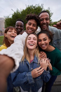 Gülümseyen selfie çeken neşeli bir arkadaş grubunun dikey fotoğrafı. Bir grup genç birlikte parkta eğleniyor tatillerde seyahatin tadını çıkarıyorlar. Yüksek kalite fotoğraf