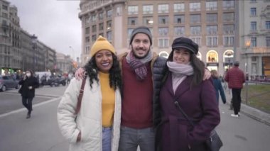 Bir grup mutlu arkadaş şehirde kış tatilinde eğleniyor. İnsanlar şapkalı ve yaralı yüzlü kameraya gülümsüyor. Yüksek kalite 4k görüntü
