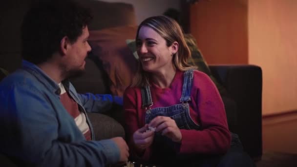 面带微笑的白种人夫妇在夜晚坐在客厅的地毯上 一边吃着爆米花一边聊天 一边看电视 千禧年男女在家中态度积极 家庭和家居 — 图库视频影像