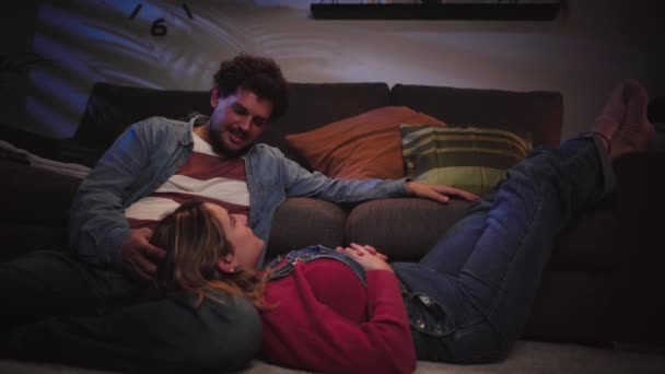 ハッピーな若い成人コーカサスカップルは 夜のリビングルームカーペットの上に座って愛情をしゃべります ミレニアル世代の男性と女性が屋内でくしゃみをする ロマンチックな関係 家族と甘い家 — ストック動画