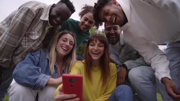 在户外用手机组微笑大学 快乐的黄色女孩和她的多民族朋友一起为自己的生活而拿着手机 社区里一代又一代的人沉迷于社交网络 低角度 — 图库视频影像