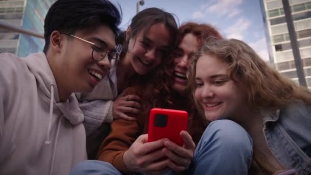 以下から携帯電話を見て4人の笑顔の友人の肖像画 大学の同級生グループは喜んで一緒にカラフルなモバイル外を使用して収集した 若い人たちは学校やSnsに戻り — ストック動画