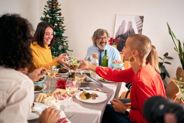 Mutlu aile evdeki Noel yemeği sırasında yemek masasının etrafında toplandı. Kadınlar geçerken salata kasesi dolusu güler yüzlü yemek alırlar. Birkaç nesildir ev hayatı ve ağaç ile şenlikli dekorasyon. 