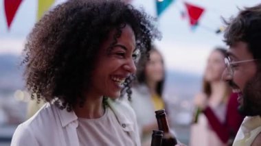 Genç, gülümseyen afro kadın ve gülen beyaz adam çatıdaki partide bira içip dans ediyor. Heyecanlı insanlar gün batımında dışarıda içerken eğleniyor. Milenyum çifti yaz tatilini kutluyor..
