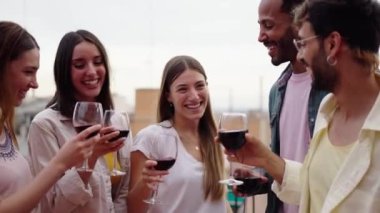 Heyecanlı, çok ırklı genç insanlar kadehlerini kaldırarak çatıda doğum günlerini kutluyorlar. Güzel arkadaşlar terasta alkollü içecekler içiyorlar. Millennial yaz tatilinin tadını çıkarıyor