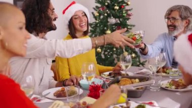 Gülen aile evdeki Noel yemeği sırasında yemek masasının etrafında toplandı. Erkekler geçerken salata kasesi dolusu gülümseyen yiyeceklerle karşıdan karşıya geçerler. Birkaç nesildir ev hayatı ve ağaç ile şenlikli dekorasyon. 